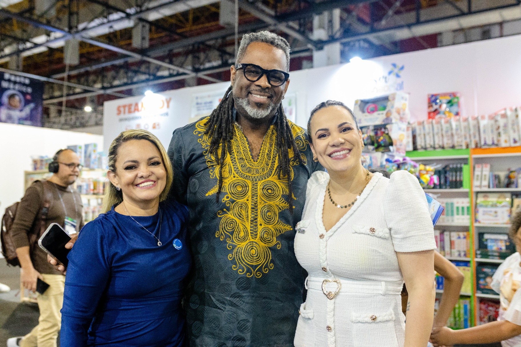 Embaixador e organizadoras sorrindo juntos na feira ExpoTEA 2025